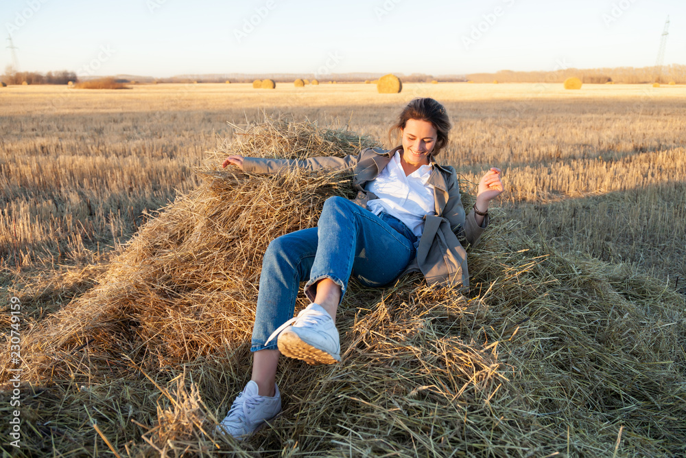 The concept of livestyle outdoor in autumn. Close up of a young woman student in a warm autumn clothes looking funny, smilling, posing, lying on haystick around field The concept of livestyle outdoor in autumn. Close up of a young woman student in a warm autumn clothes looking funny, smilling, posing, lying on haystick around field