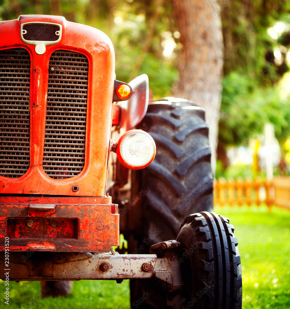 Fototapeta premium Croppped photo of old vintage red tractor standing on a farm field at sunset.