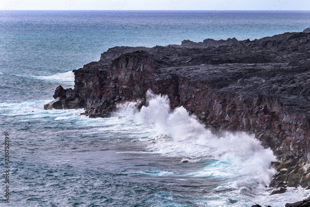Large waves crashing against tall volcanic clifs on Hawaii's Big Island, Below Chain of Craters road in Volcano National Park. Pacific ocean and sky in the background.