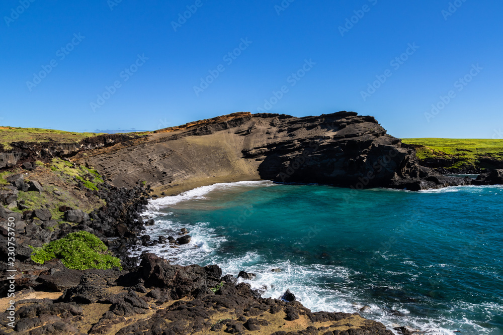 Green sand beach (papakolea) near South Point on Hawaii's Big Island. Beach is at the bottom of the steep slope; blue-green ocean, rocky shoreline is in the foregound.