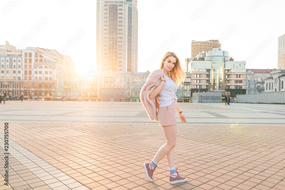 Fashionable pretty girl in pink clothes poses on the street and looks at the camera. Street portrait of a stylish teenage girl in pink clothes against the background of the city and the sunset Fashionable pretty girl in pink clothes poses on the street and looks at the camera. Street portrait of a stylish teenage girl in pink clothes against the background of the city and the sunset