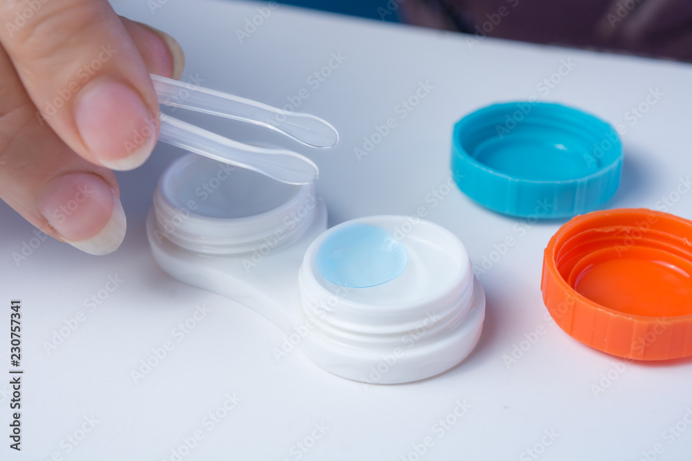 The hand with help of forceps pulls the lenses out of the container. The hand with help of forceps pulls the lenses out of the container.