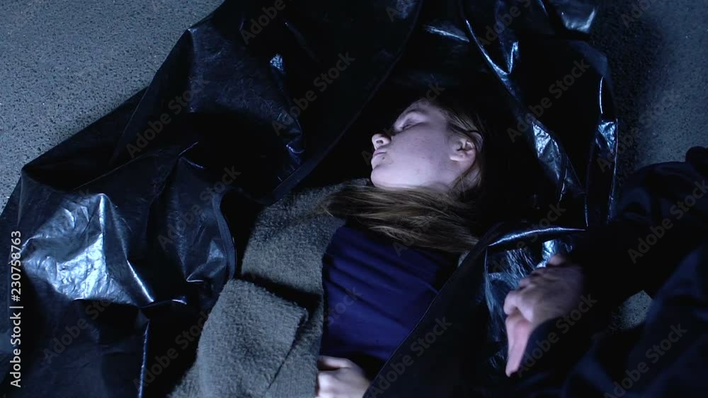 Dead young woman in body bag at crime scene, police officer examining