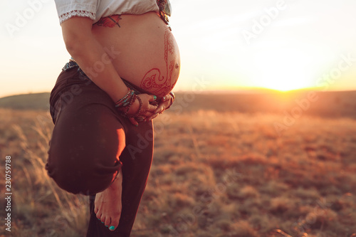 Pregnant woman doing yoga in the field at sunset.