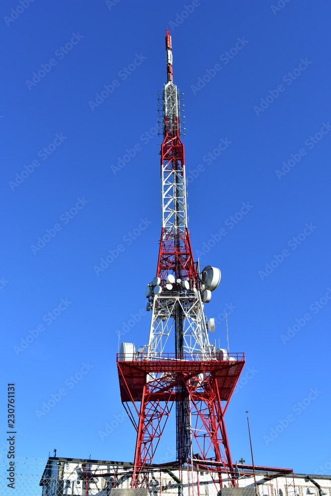 Red and white telecommunications tower. Shiny antenna, blue sky, sunny day. Red and white telecommunications tower. Shiny antenna, blue sky, sunny day.