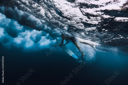 Professional surfer with surfboard dive underwater with big ocean wave.