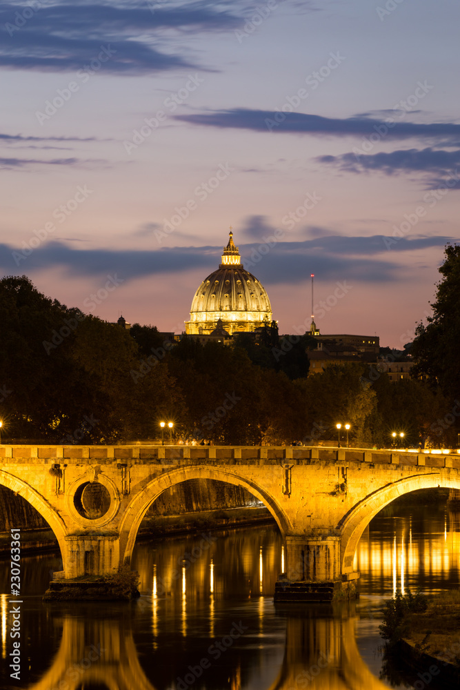 Fototapeta premium Illuminated Dome of St. Peter's Basilica, bridge and the Tiber river at a beautiful sunset in Rome, Italy