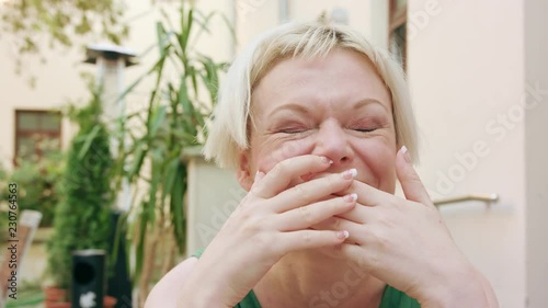 A pretty young blonde woman wearing a green dress sitting outside laughing outloud. Close-up shot photo