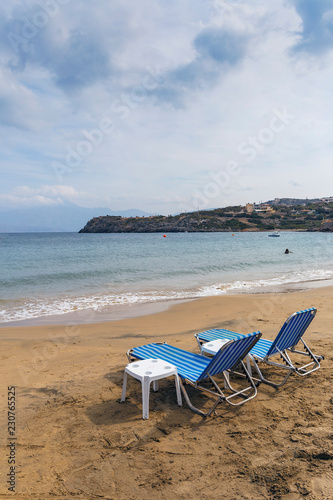 lounge chairs with tables on a sandy beach against the background of the mountains and sky with clouds