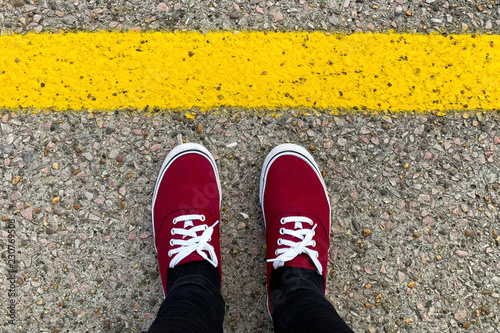 Red sneakers in front of the yellow line. Safety concept