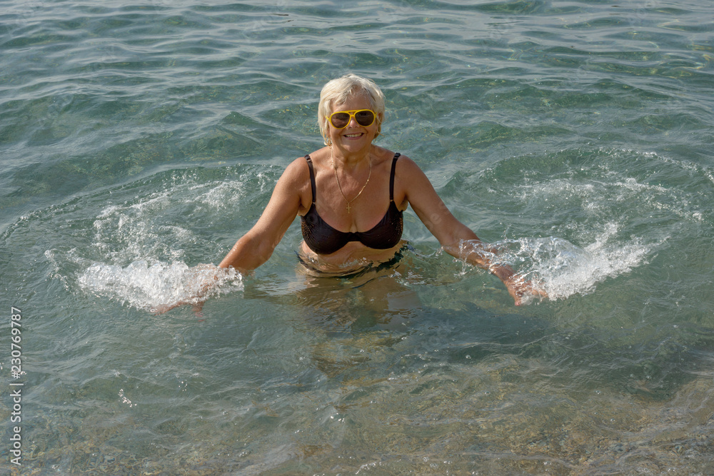 Aged woman is doing splashing motions in clear sea water.