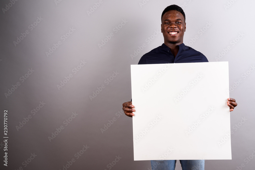 Young African businessman holding white board against white back Young African businessman holding white board against white back