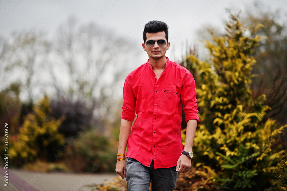 Obraz premium Indian man at red shirt and sunglasses posed outdoor.