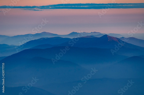 Beautiful morning alpine landscape with tonal perspective. Ponk and blue tonality mountains with foggy valleys © Mny-Jhee