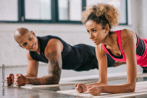 attractive african american sportswoman doing plank with her boyfriend at gym
