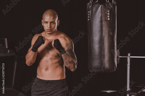 Serious African American boxer posing in fight position near punching bag at gym © LIGHTFIELD STUDIOS