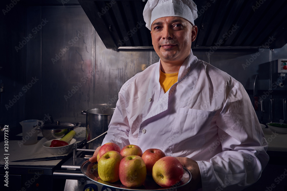 Chef cook in a white apron and cooks hat on a kitchen Chef cook in a white apron and cooks hat on a kitchen