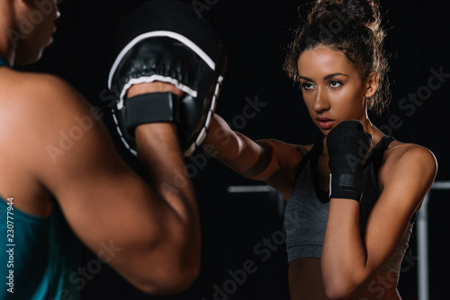 partial view of male personal trainer exercising with female boxer at gym