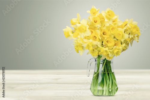 Narcissus flowers in vase on wooden background