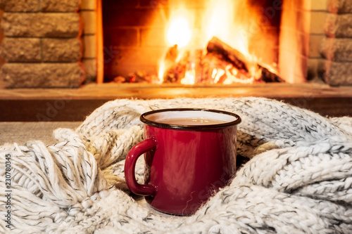 Cozy scene near fireplace with a Red enameled mug with hot tea and cozy warm scarf.