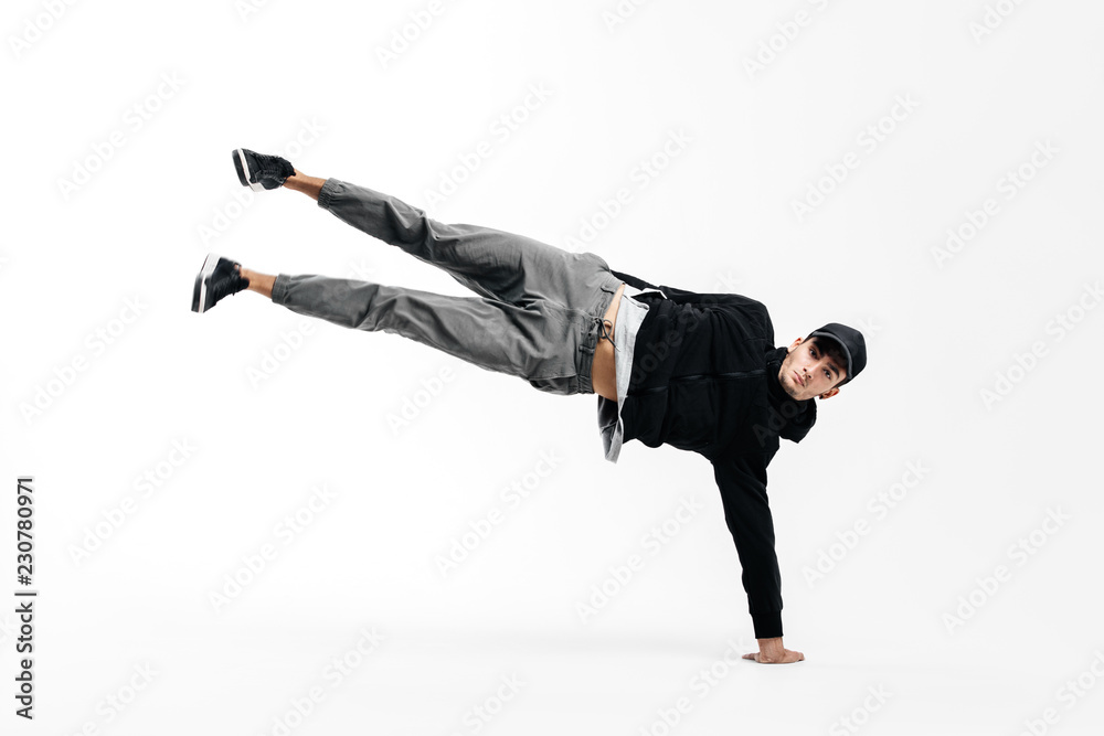 Stylish young dancer is dancing breakdance. He is standing on one arm and lifting both legs up.