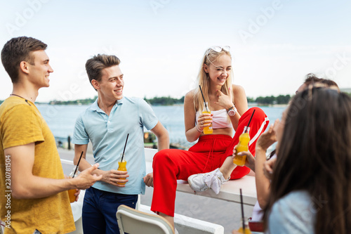 A company of good-looking friends laughing and drinking yellow cocktails and socialising in the nice cafe next to the river. Cheers. Entertainment, having good time. River is in the background.