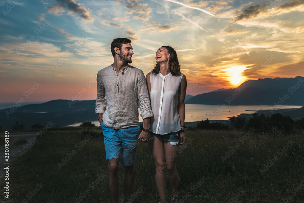 Portrait of young couple having good times in nature behind them is a beautiful sunset over Boka Bay
