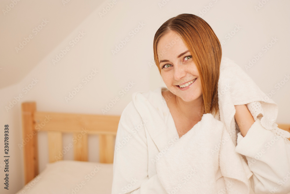 Lovely female with wet hair, dries head with towel, being pleased after taking bath, dressed in white bathrobe, poses against white background Lovely female with wet hair, dries head with towel, being pleased after taking bath, dressed in white bathrobe, poses against white background