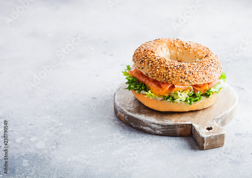 Fresh healthy bagel sandwich with salmon, ricotta and lettuce on vintage chopping board on stone kitchen table background. Healthy diet food. Space for text