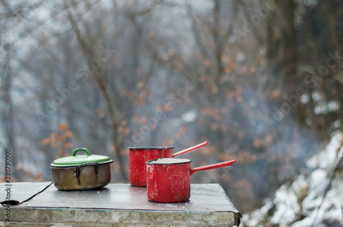 Enamel dishes on the table - cooking outdoors in the winter by campfire photo