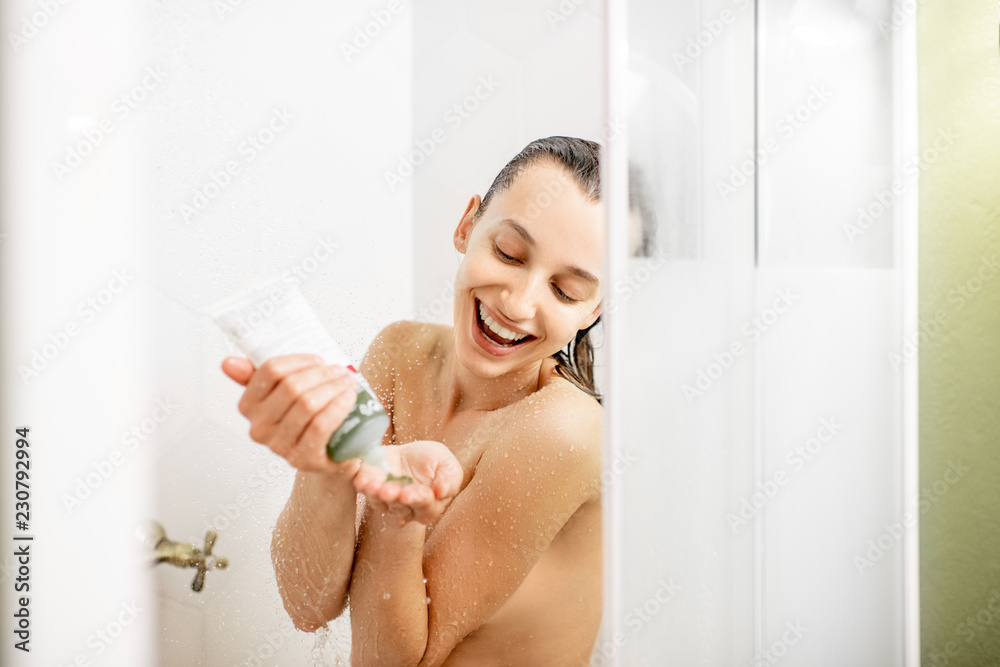 Happy woman pouring shampoo from the tube, while taking shower in the white shower cabin Happy woman pouring shampoo from the tube, while taking shower in the white shower cabin