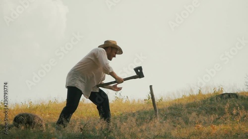 A farmer beat a stake into the ground. Dog walks around him.