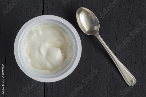 Yogurt in plastic cup on rustic black table with small silver spoon - natural Greek yoghurt top view photo