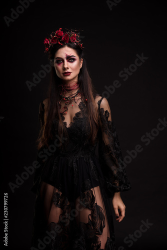 Portrait of a girl in the image for Halloween. Black Widow. Wreath of roses. Makeup for halloween. Eyes like gimlets. Black lace dress. Black background.