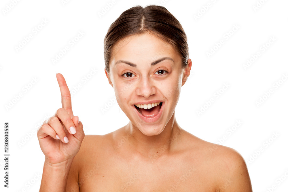 Portrait of young beautiful happy woman with no makeup pointing up on white backgeound
