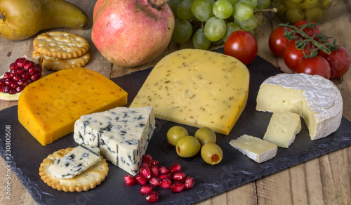 Cheese board with three cheeses, gouda with pimento, gouda with cumin seeds and roquefort blue cheese  and camembert close up on rustic wooden background