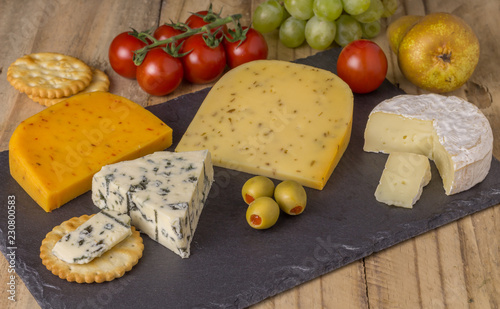 Cheese board with three cheeses, gouda with pimento, gouda with cumin seeds and roquefort blue cheese  and camembert close up on rustic wooden background