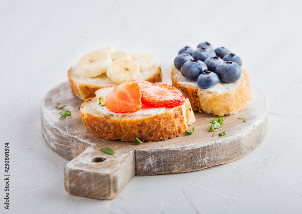 Fresh healthy mini sandwiches with cream cheese, fruits and berries on vintage wooden board. Strawberries, blueberries, bananas and raspberries on stone kitchen table background.Top view. Fresh healthy mini sandwiches with cream cheese, fruits and berries on vintage wooden board. Strawberries, blueberries, bananas and raspberries on stone kitchen table background.Top view.