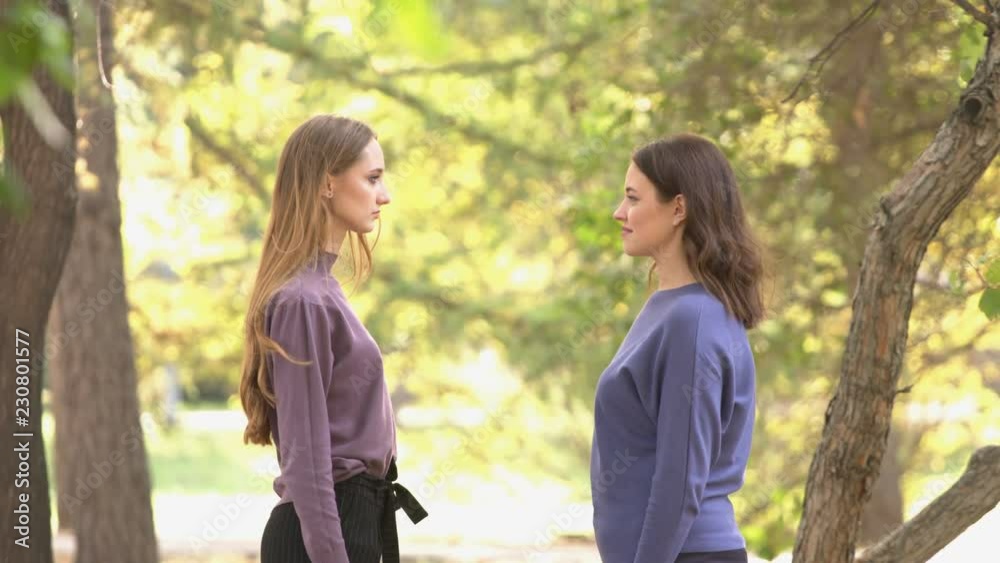 Girls in park.
Relationship between girls. Girls stand opposite each other and look into their eyes. After that, girl on the right begins to laugh. Good weather in park.