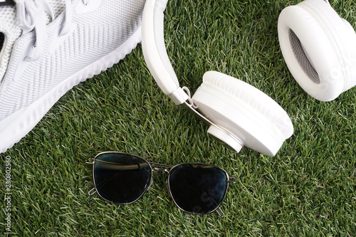 Fitness or healthy lifestyle concept. White running shoes, headphones and smartphone on a grass.