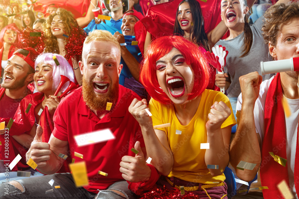 Young sport supporter happy fans cheering at stadium. Group of young woman and man support the football team during the match