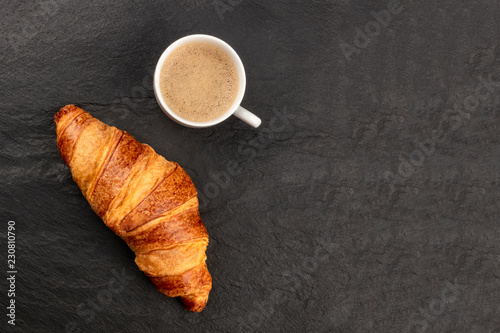 Morning Coffee Time. A photo of a croissant with a cup of coffee  shot from the top on a black background with a place for text