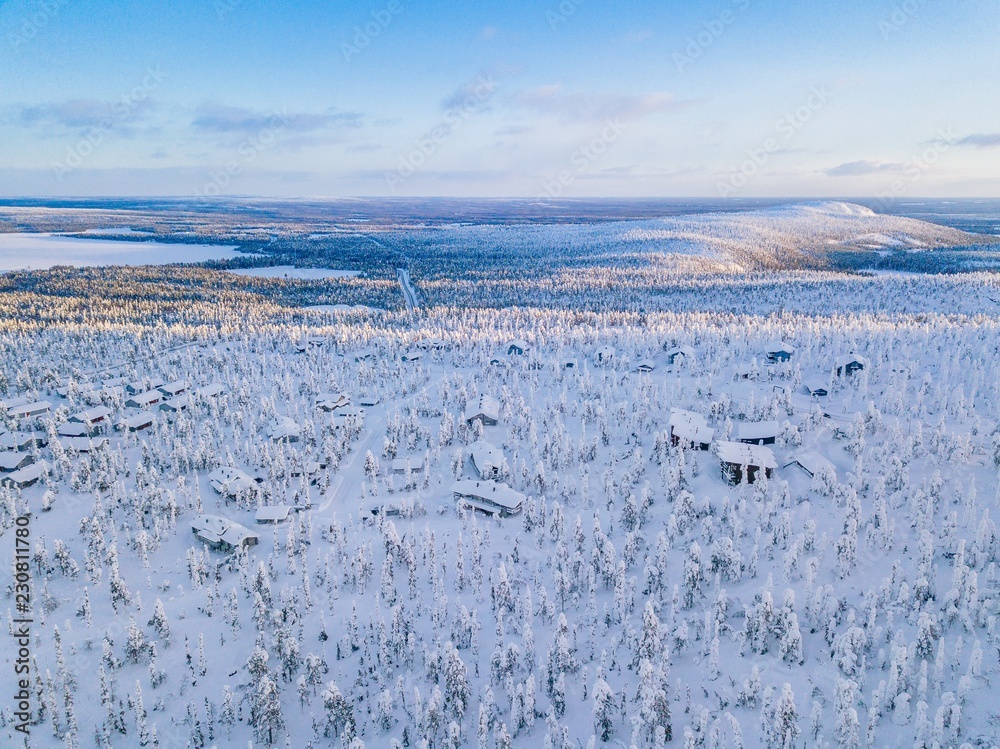Aerial view of winter forest with frosty trees, rural road and village in Finland