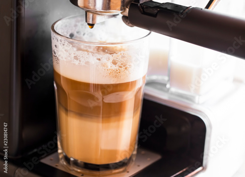 Coffee machine making latte coffee in a transparent glass with milk froth, delicious coffee