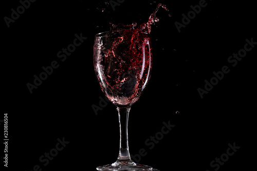 Red wine falls into a glass and creates splash and splashes on a black background.
