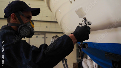 Professional master man in a robe and puller with spray gun puts a layer of paint or ceramics on the yacht. Concept of: Dangerous work, Chemistry, Paints, Garage, Transport Service.