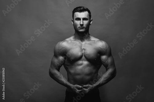 Bodybuilding. Strong man posing on background. Athletic young boy showing muscles.