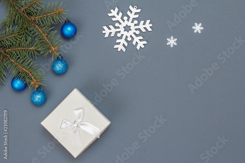 Gift box, fir tree branches with toy balls, snowflackes on gray background