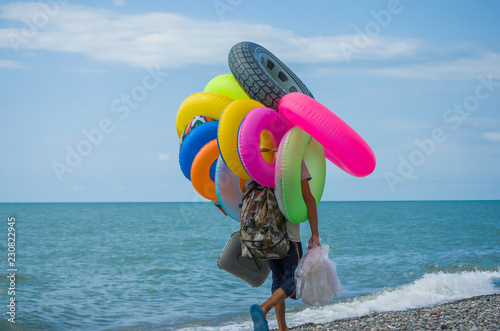 Unknown seller of inflatable toys and swimming laps goes along the beach
