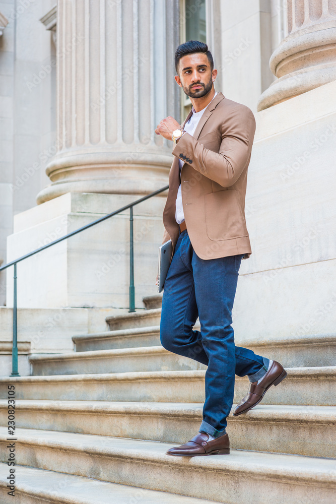 After work, Young East Indian American Businessman with beard, wearing brown  blazer, white round collar shirt, blue pants, black leather shoes, walking  down stairs from office building, looking away.. Photos | Adobe